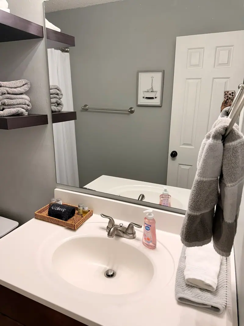 Rental bathroom staged with folded towels on floating shelves and a stocked vanity