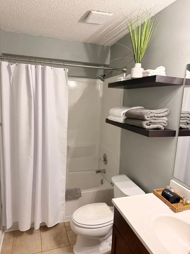 Rental bathroom with a white shower curtain and towels stacked on the shelves