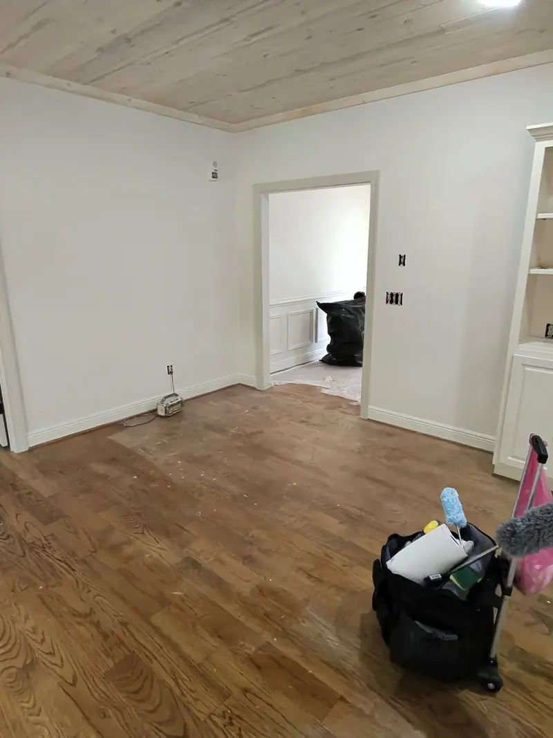 Empty room with hardwood floors and a cleaning cart, midway through a move-out clean