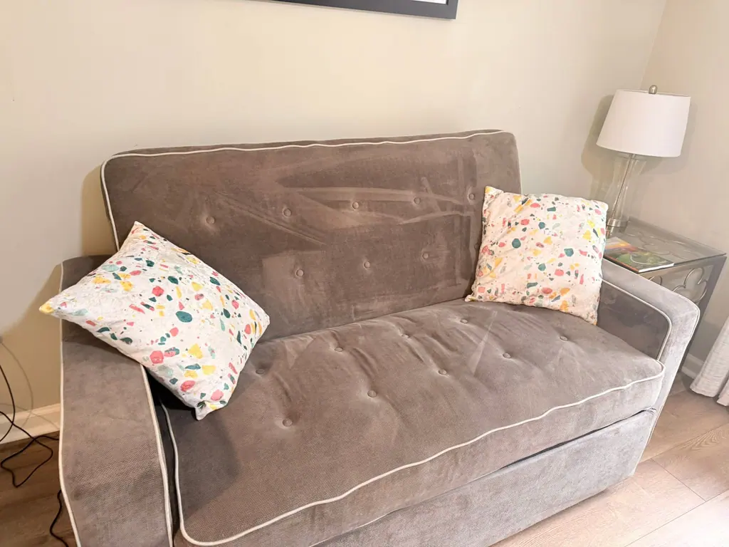 Staged living room corner with a gray loveseat, patterned pillows and a lamp, freshly cleaned