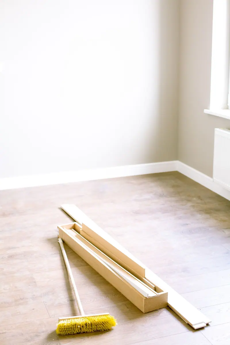 Broom and spare planks in a bright, empty room after renovation work